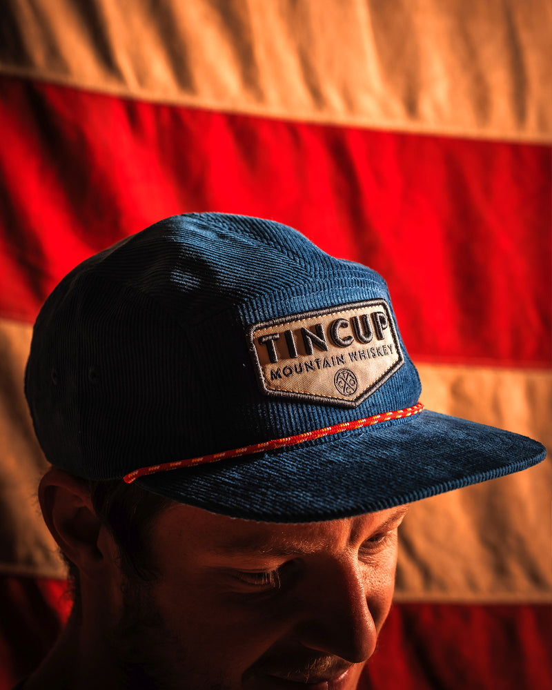 Navy Blue TINCUP Navy Camper Hat on model in front of red and white background